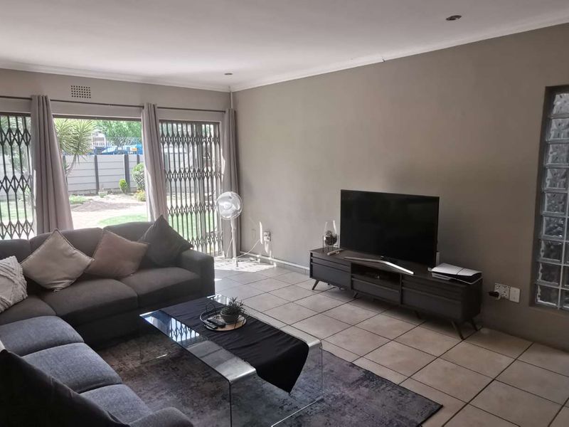 A living room featuring tiled flooring, recessed downlighting, and a unique glass block feature wall, with direct access to the exterior through sliding security doors.