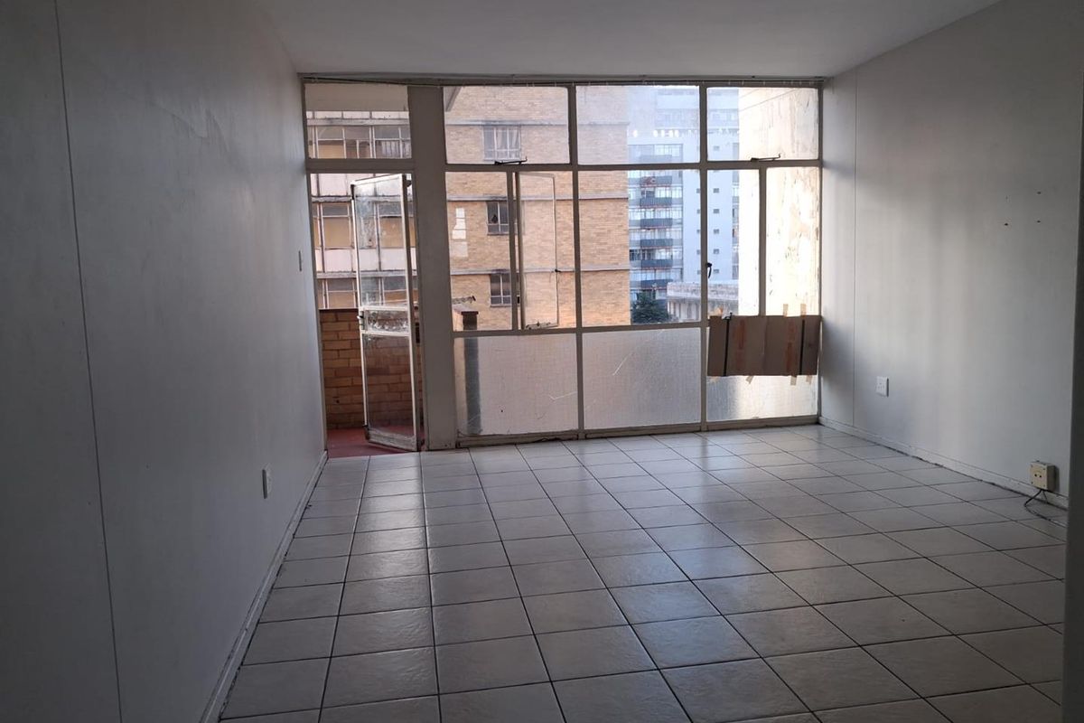 An empty living room featuring tiled flooring and a large glass window wall with direct access to a balcony.