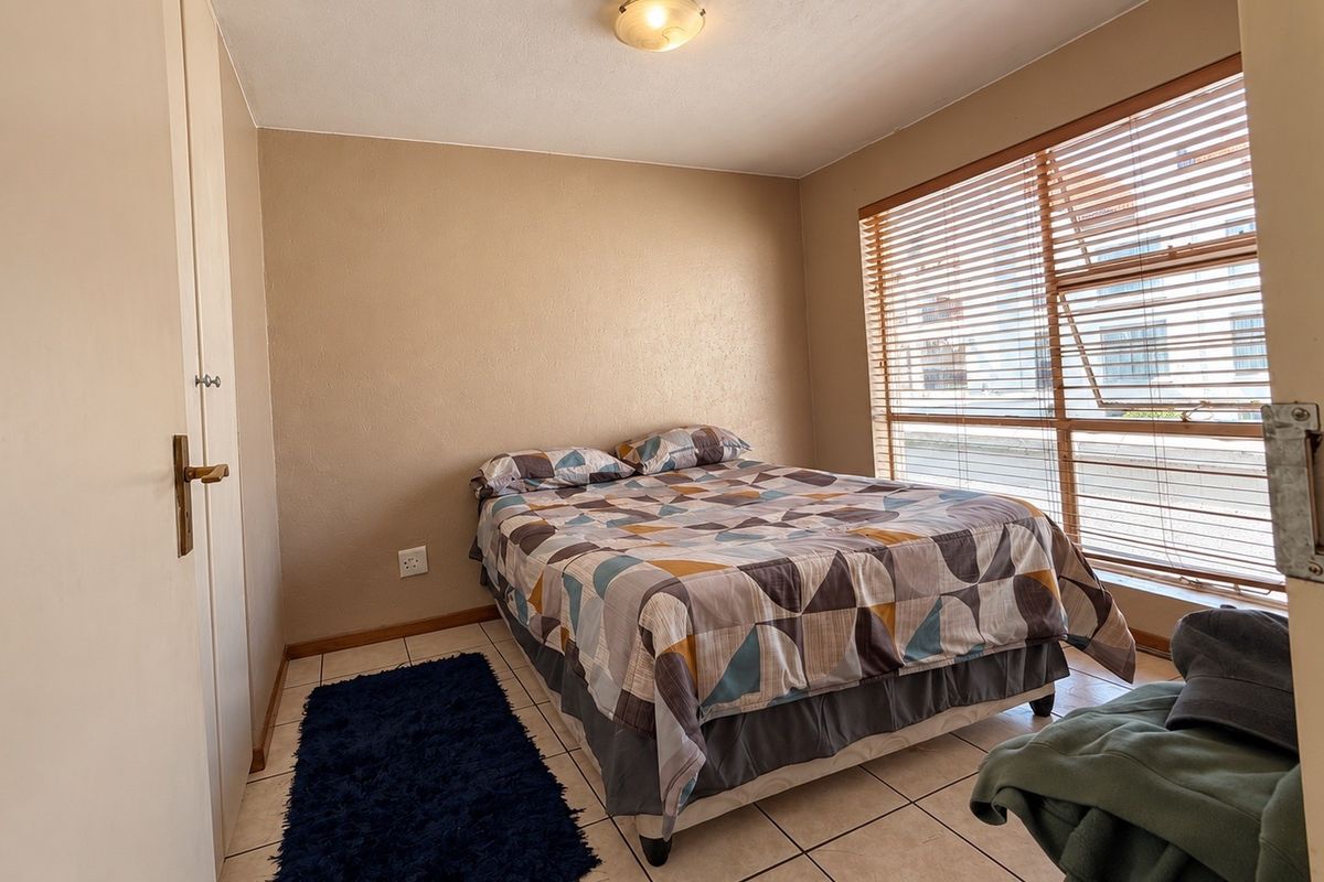 A functional bedroom featuring tiled flooring, a built-in cupboard, and large windows with venetian blinds, offering a neutral canvas for potential updates.