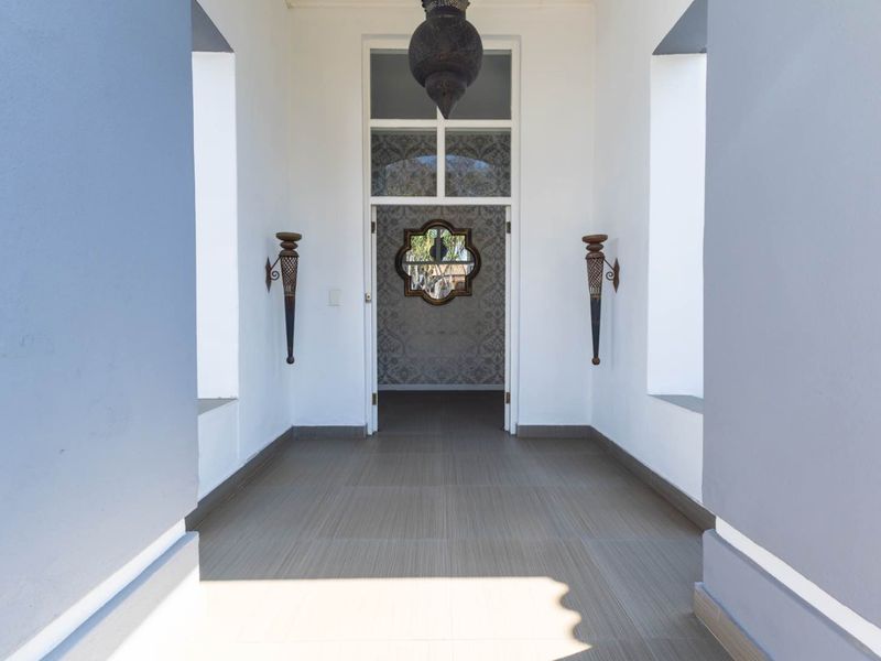 A bright and welcoming entrance hall featuring tiled flooring, high ceilings with a decorative pendant light, and elegant wall-mounted fixtures.