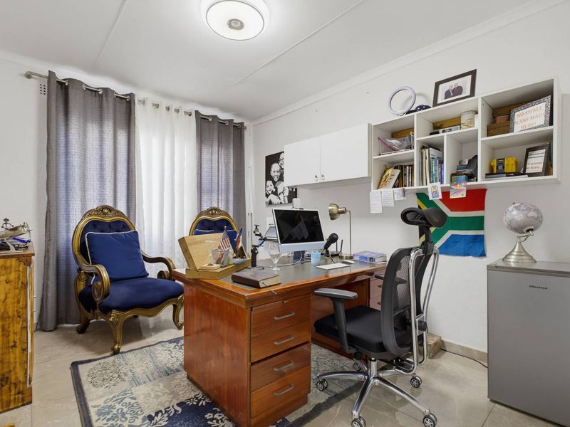 A functional home office space featuring built-in wall cabinetry and shelving, tiled flooring, and ample natural light from the window.