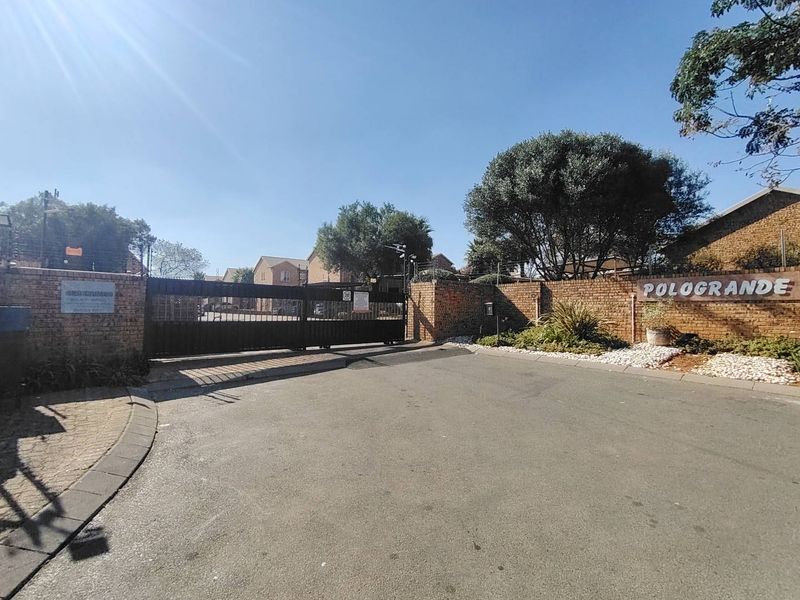 The entrance to the Pologrande complex featuring a secure automated sliding gate, brick boundary walls, and electric fencing.