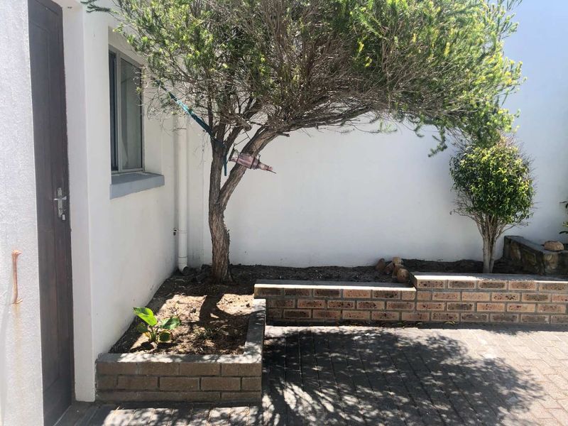 A private rear courtyard featuring brick planter boxes, paved flooring, and direct access to the townhouse interior.