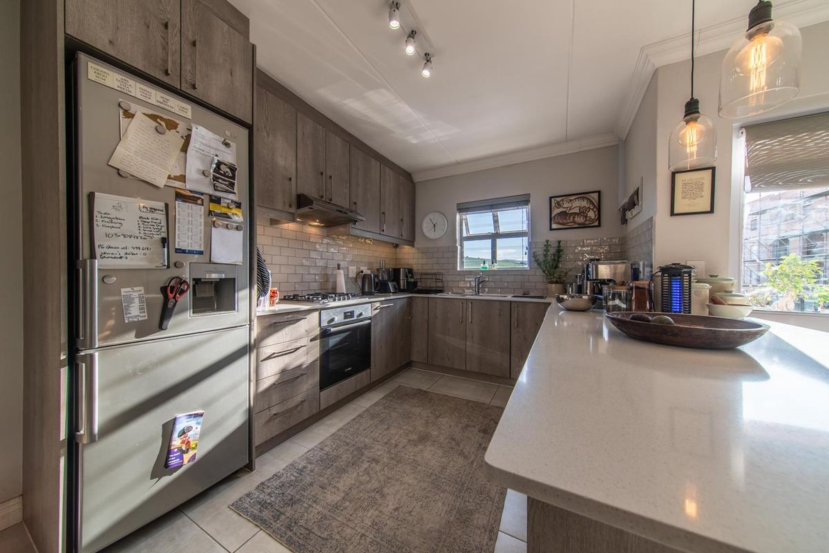 Modern kitchen featuring wood-grain cabinetry, stone countertops, subway tile backsplash, and integrated appliances, complemented by stylish pendant and track lighting.