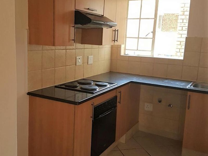 A functional kitchen featuring laminate cabinetry, black countertops, built-in oven and hob, and tiled flooring. The space is ready for a modern update.