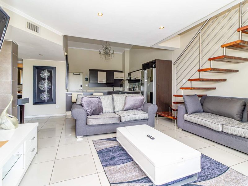 Spacious open-plan living area featuring modern tiled floors, a striking floating staircase, and an integrated kitchen with contemporary cabinetry.