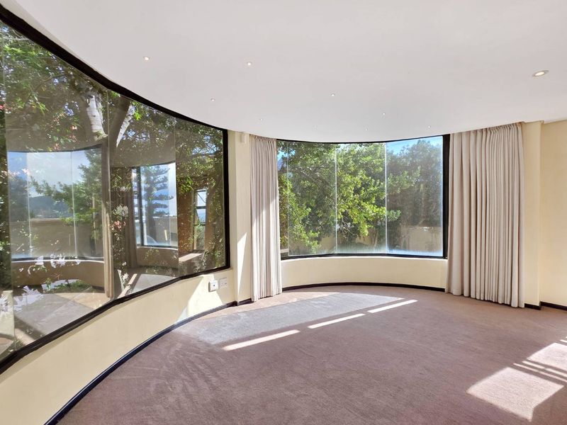 Spacious living area featuring expansive curved floor-to-ceiling windows that provide abundant natural light and pleasant garden views.