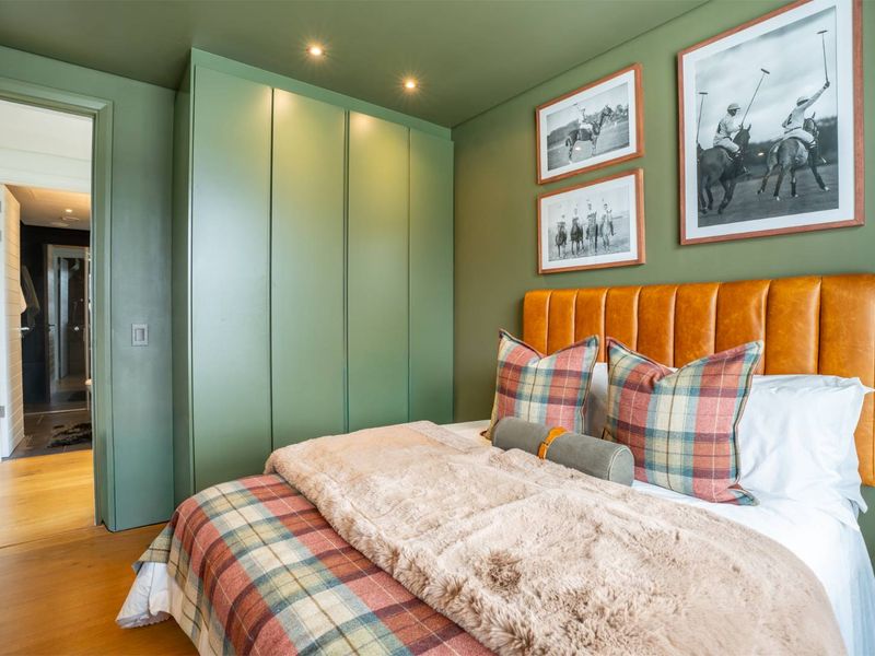 A well-appointed bedroom featuring custom floor-to-ceiling built-in wardrobes, recessed downlighting, and warm hardwood flooring, with a seamless transition to an adjoining bathroom.