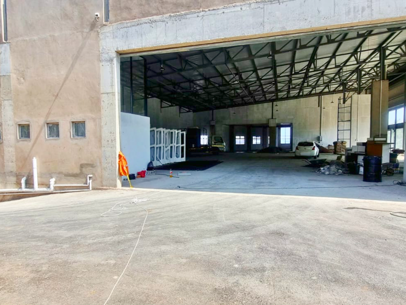 Large industrial warehouse space featuring high ceilings with exposed steel trusses, concrete flooring, and a wide access opening for heavy vehicle entry.