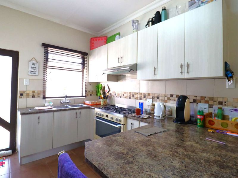 Functional kitchen featuring laminate cabinetry, gas hob with extractor fan, tiled backsplash, and ample countertop space with direct access to the exterior.