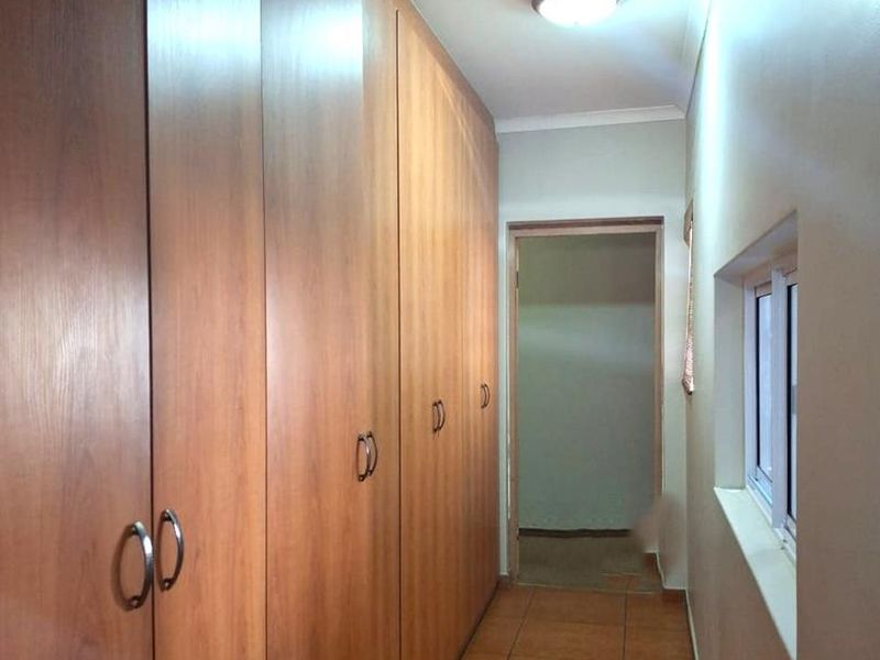 A functional hallway featuring extensive built-in wooden cabinetry for storage, tiled flooring, and a window providing natural light.