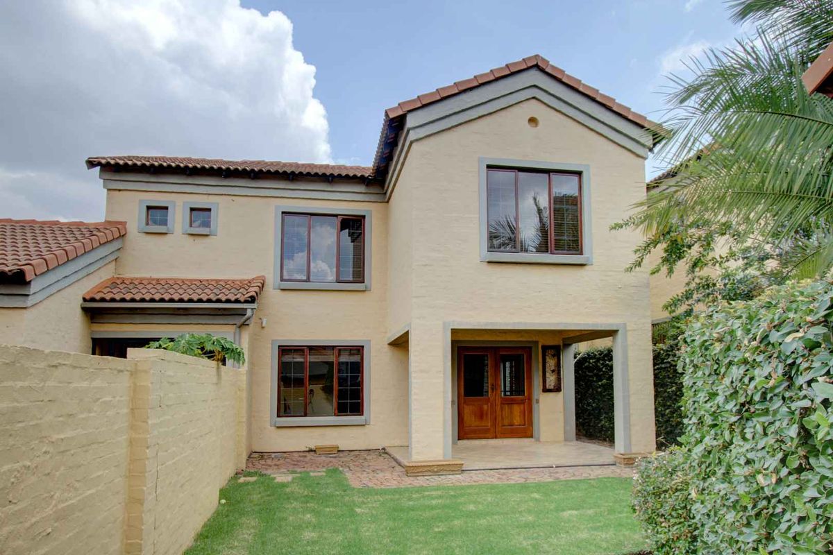 Rear view of a double-story townhouse featuring a covered patio, paved outdoor area, small garden, and timber-framed windows.