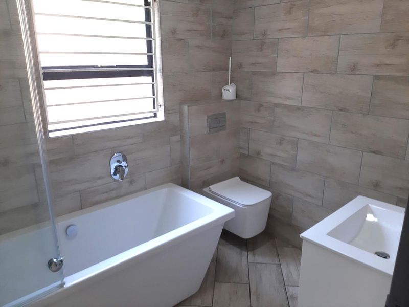 Modern bathroom featuring a freestanding bathtub, wall-mounted toilet with concealed cistern, vanity basin, and contemporary wood-look wall and floor tiling.