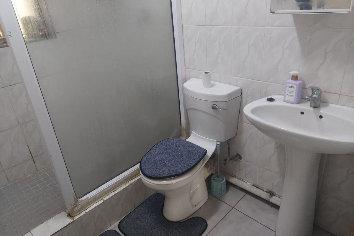 A functional bathroom featuring a pedestal sink, toilet, and a glass-enclosed shower with tiled finishes throughout.