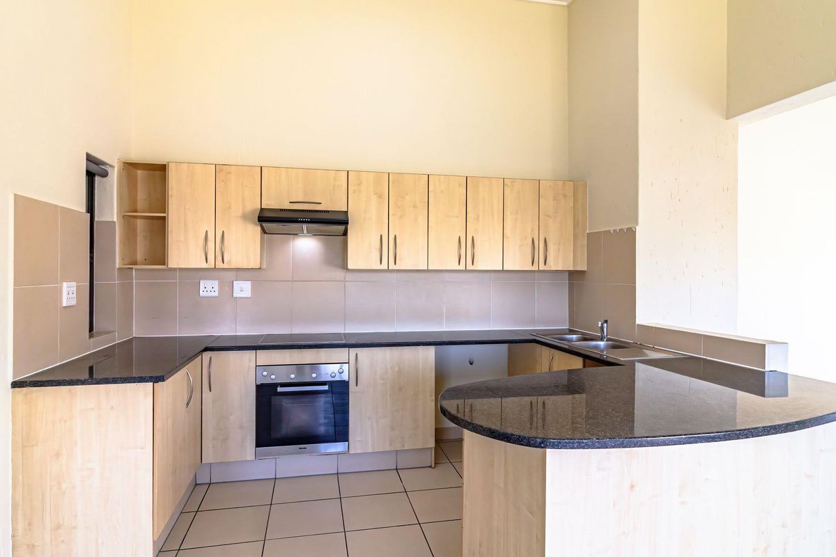 A clean, empty kitchen featuring light wood cabinetry, dark granite countertops, a built-in oven, hob, extractor fan, and a breakfast bar peninsula.
