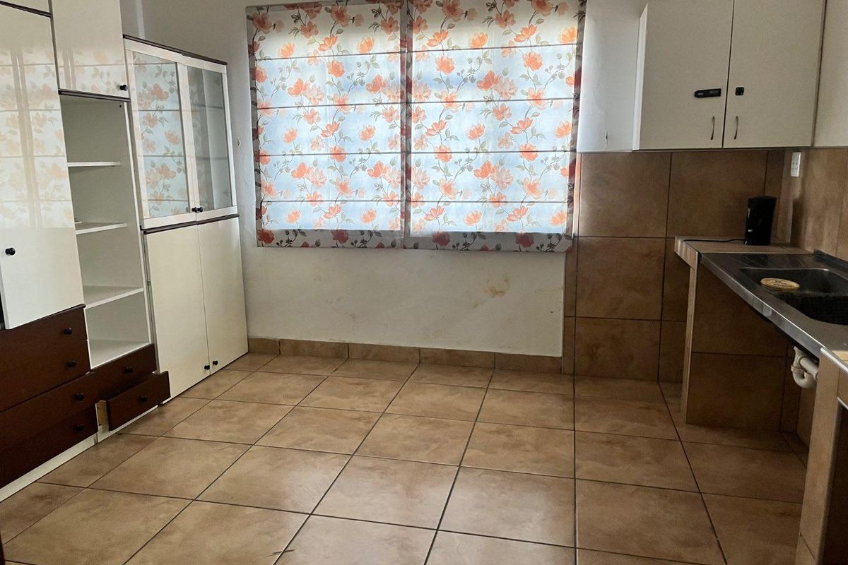 A functional kitchen area featuring tiled flooring, built-in cabinetry, and a stainless steel sink with tiled splashback.