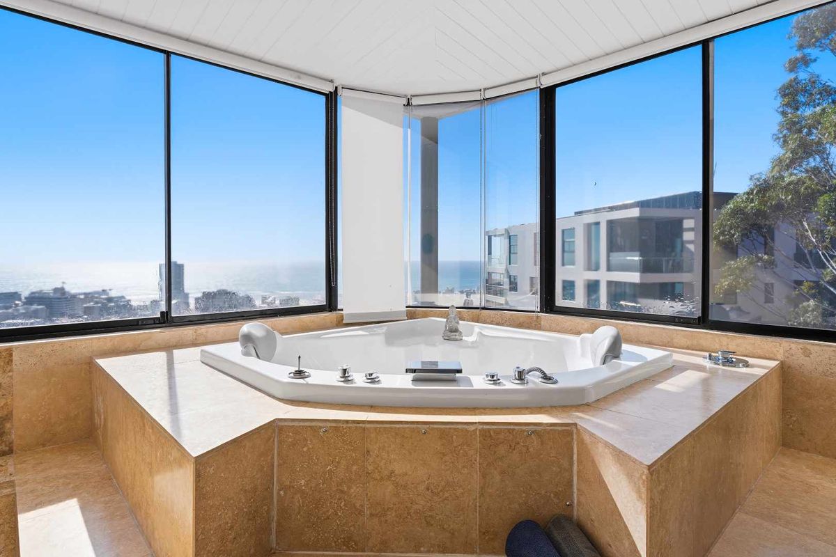 Luxurious bathroom featuring a built-in corner spa bath set against expansive floor-to-ceiling windows with panoramic ocean and city views.