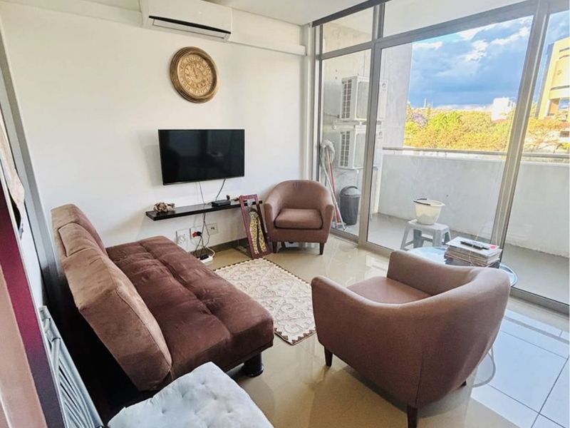 A compact living room featuring tiled flooring, a wall-mounted air conditioning unit, and large floor-to-ceiling glass doors providing access to a balcony.
