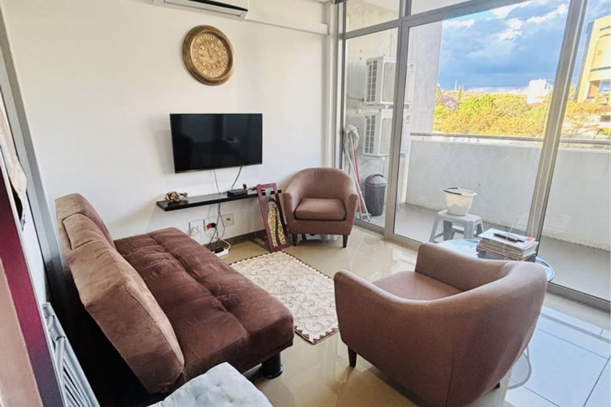 A compact living room featuring tiled flooring, a wall-mounted air conditioning unit, and large floor-to-ceiling glass doors providing access to a balcony.
