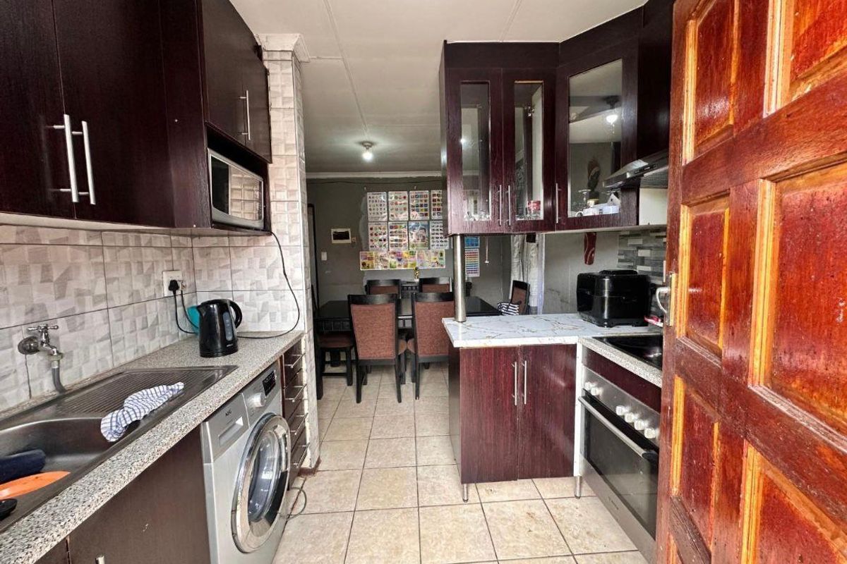 A functional kitchen featuring dark wood cabinetry, integrated oven and hob, tiled splashbacks, and a dedicated laundry space with a built-in washing machine.
