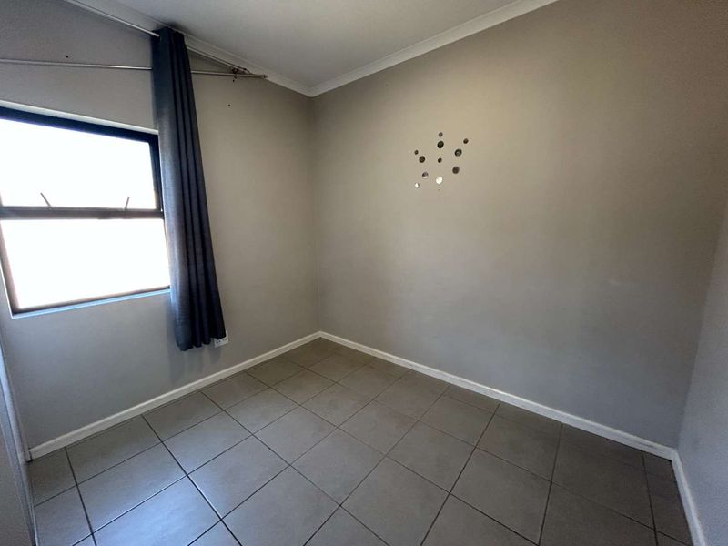 An empty bedroom featuring neutral grey walls, tiled flooring, and a single window with a curtain rod.