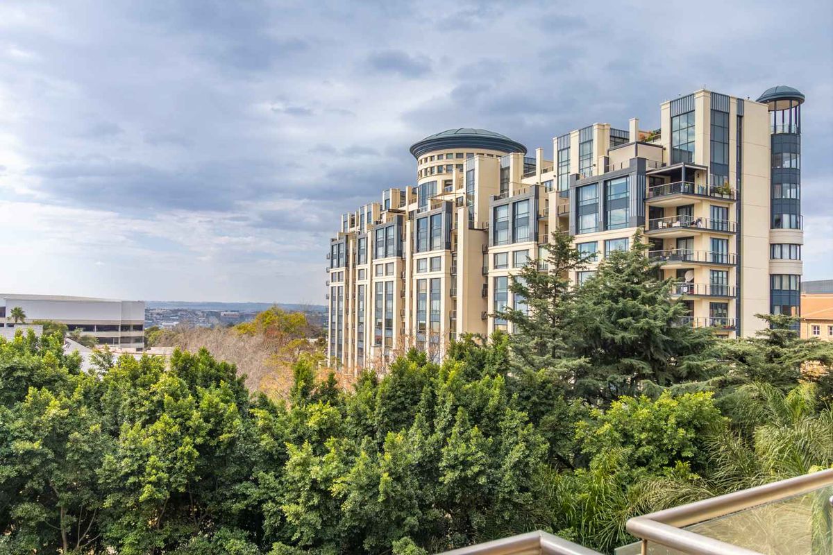 A view of the penthouse building exterior, showcasing its architectural design, multiple balconies with glass balustrades, and surrounding mature trees.