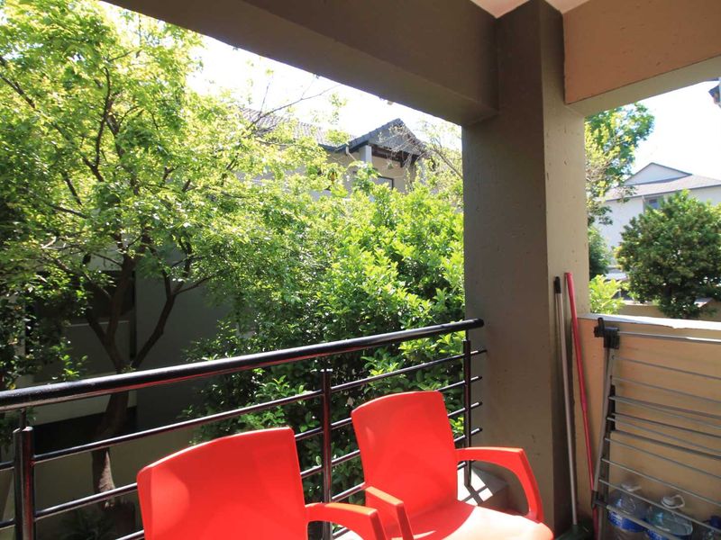 A covered balcony featuring a metal balustrade and views of surrounding trees and neighboring residential buildings.