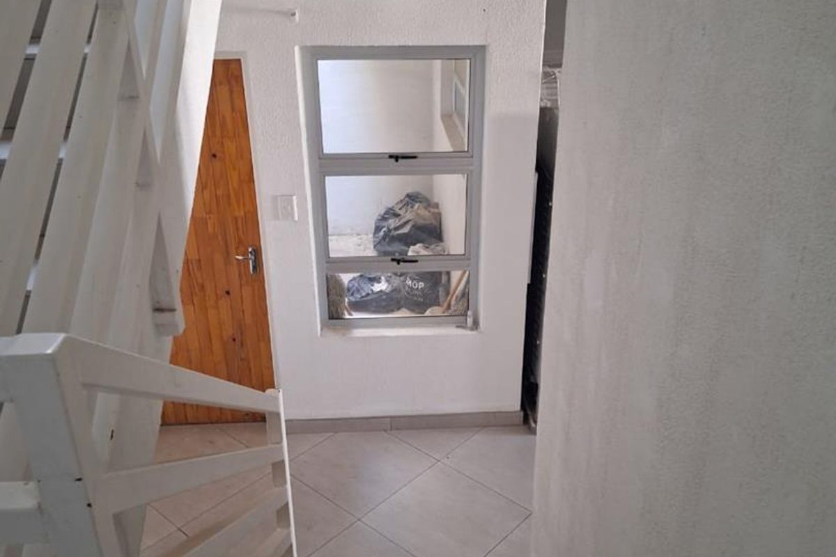 A functional hallway area featuring a staircase with white railings, tiled flooring, and a wooden door leading to an adjacent space.