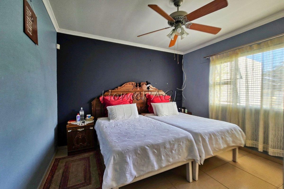 A bedroom featuring tiled flooring, a ceiling fan, and a dark accent wall, providing a functional space with natural light.