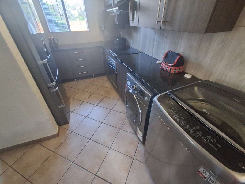 A functional galley-style kitchen featuring dark cabinetry, granite countertops, tiled flooring, and integrated appliance spaces.
