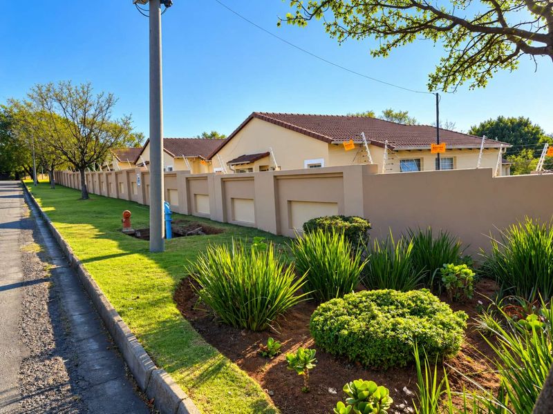 A well-maintained townhouse complex exterior featuring a solid perimeter wall, electric fencing, and neatly landscaped verge with a tiled roof profile.