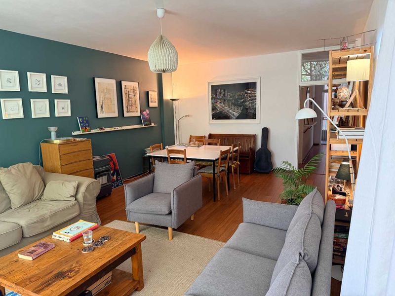 An open-plan living and dining area featuring hardwood flooring, a striking teal accent wall, and neutral decor, creating a warm and inviting atmosphere.
