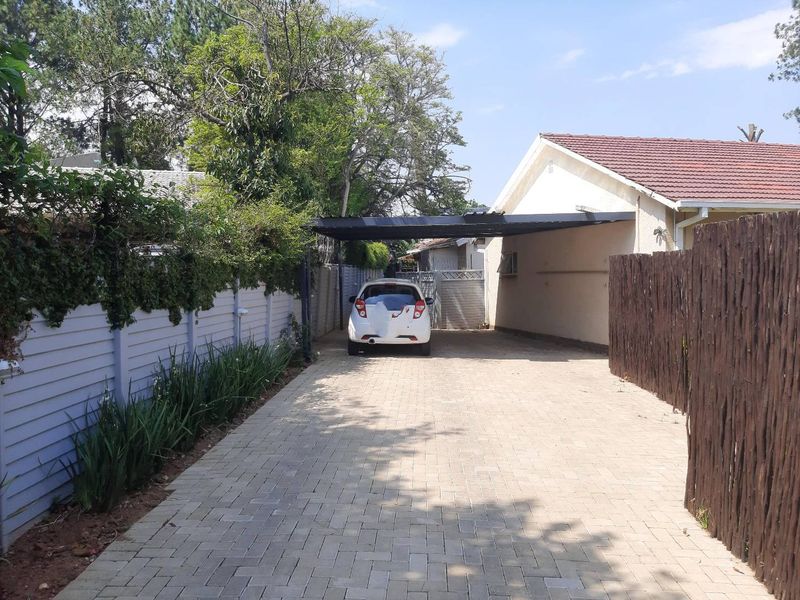 A paved driveway leading to a carport, featuring a combination of timber fencing and precast walling along the property boundary.