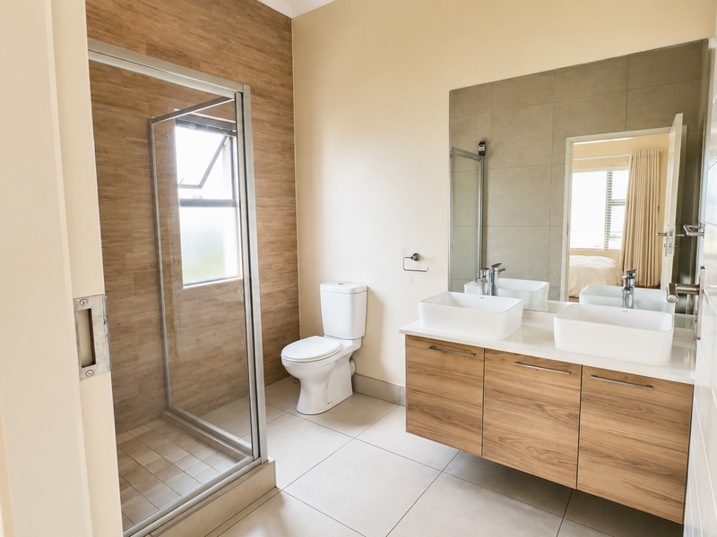 Modern bathroom featuring a double vanity with vessel sinks, a floating wood-finish cabinet, and a spacious walk-in shower with glass enclosure.