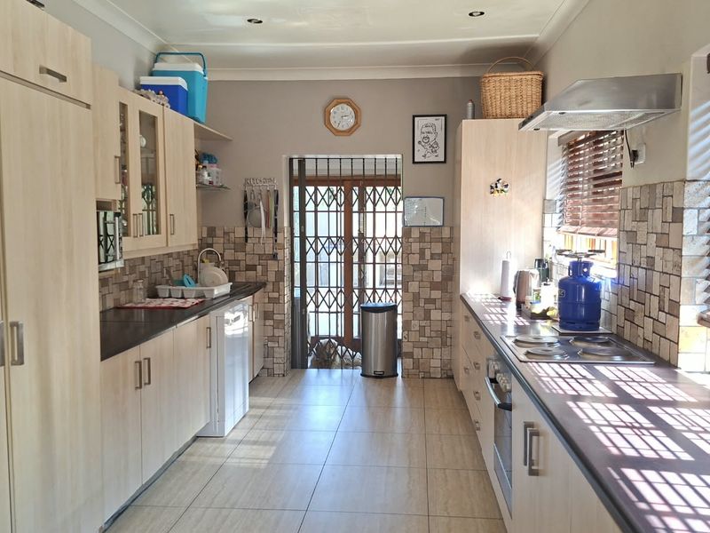 A functional galley-style kitchen featuring light wood cabinetry, tiled backsplash, built-in oven and hob, and tiled flooring with a rear security door.