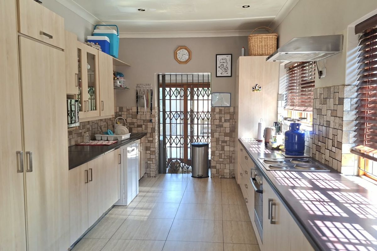 A functional galley-style kitchen featuring light wood cabinetry, tiled backsplash, built-in oven and hob, and tiled flooring with a rear security door.