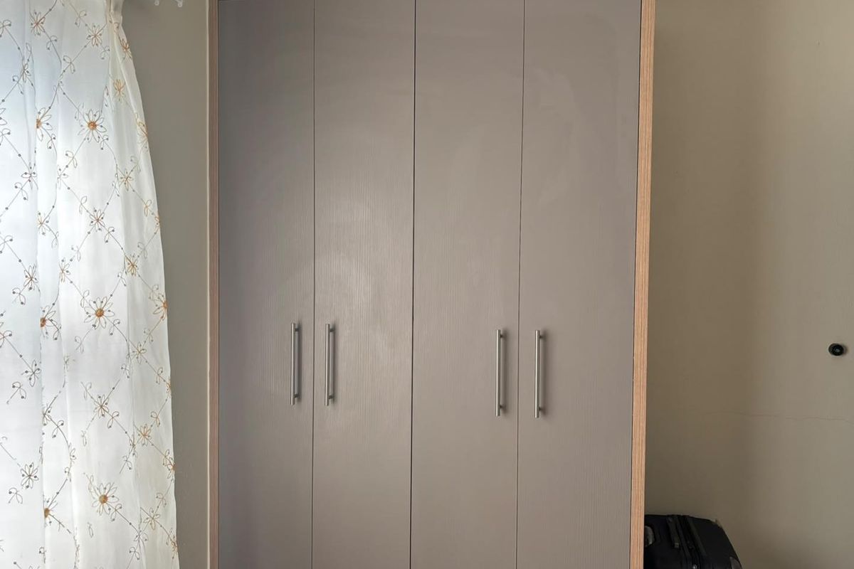 A bedroom featuring a modern, light-toned built-in wardrobe with sleek metal handles.