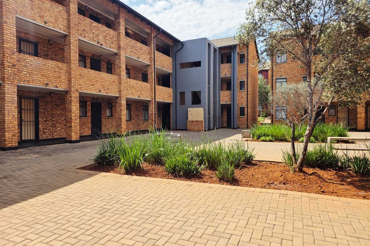 A well-maintained apartment complex courtyard featuring face brick architecture, paved walkways, and established garden beds.