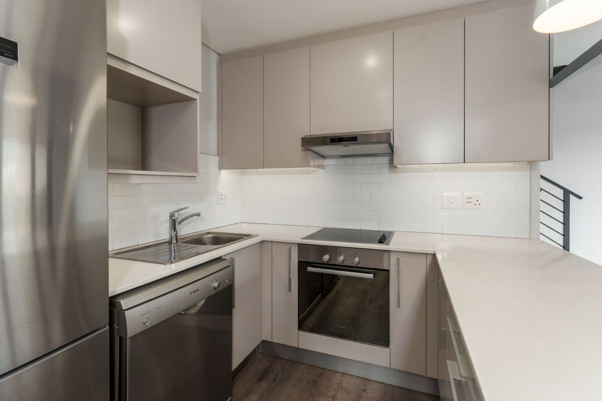 Modern kitchen featuring sleek cabinetry, stone countertops, subway tile backsplash, and integrated stainless steel appliances including an oven, hob, and extractor fan.