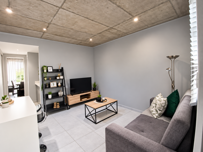 Modern open-plan living area featuring an exposed concrete ceiling, recessed lighting, and neutral tiled flooring, creating a contemporary and well-lit space.