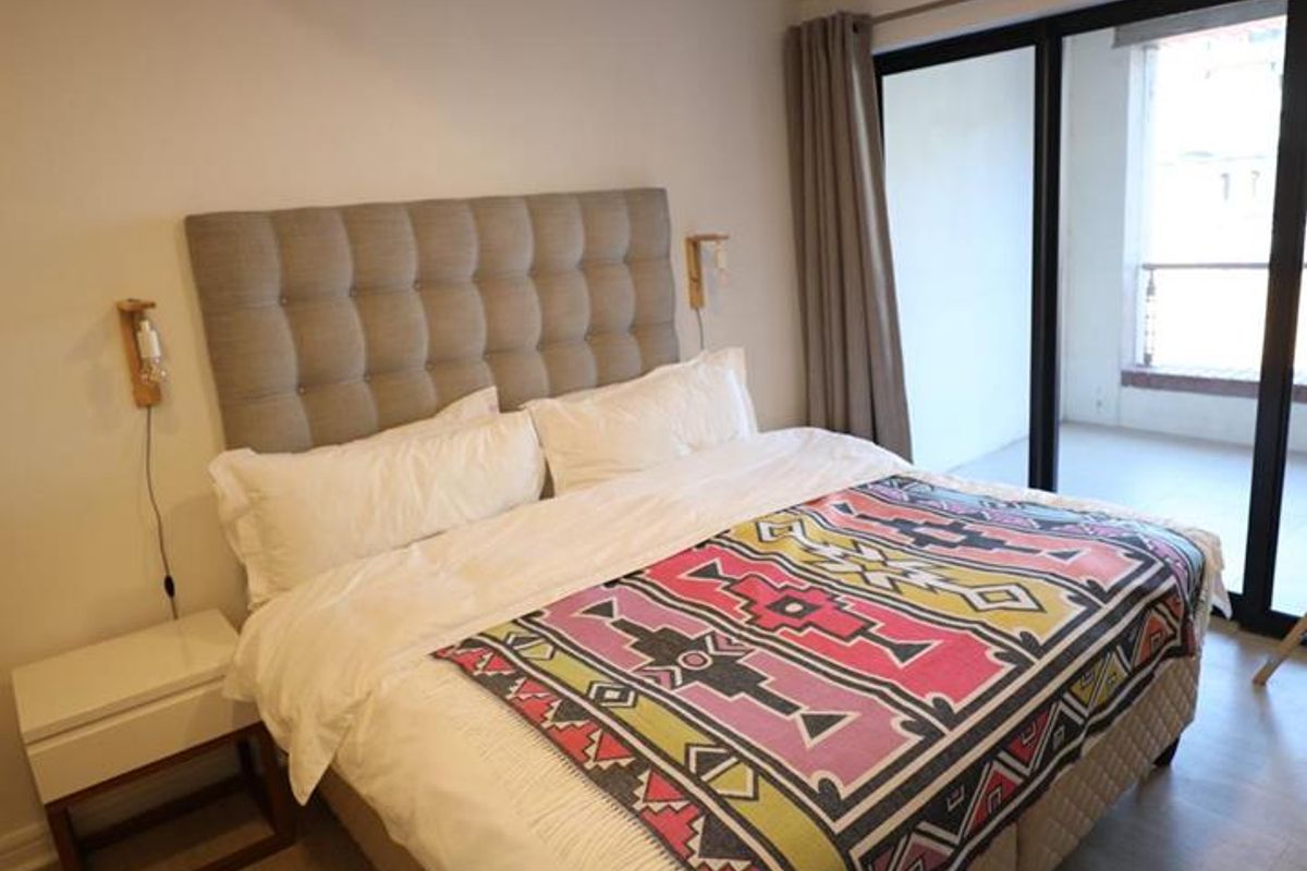 A well-maintained bedroom featuring light wood-look flooring, modern recessed lighting, and large sliding glass doors providing access to a private balcony.
