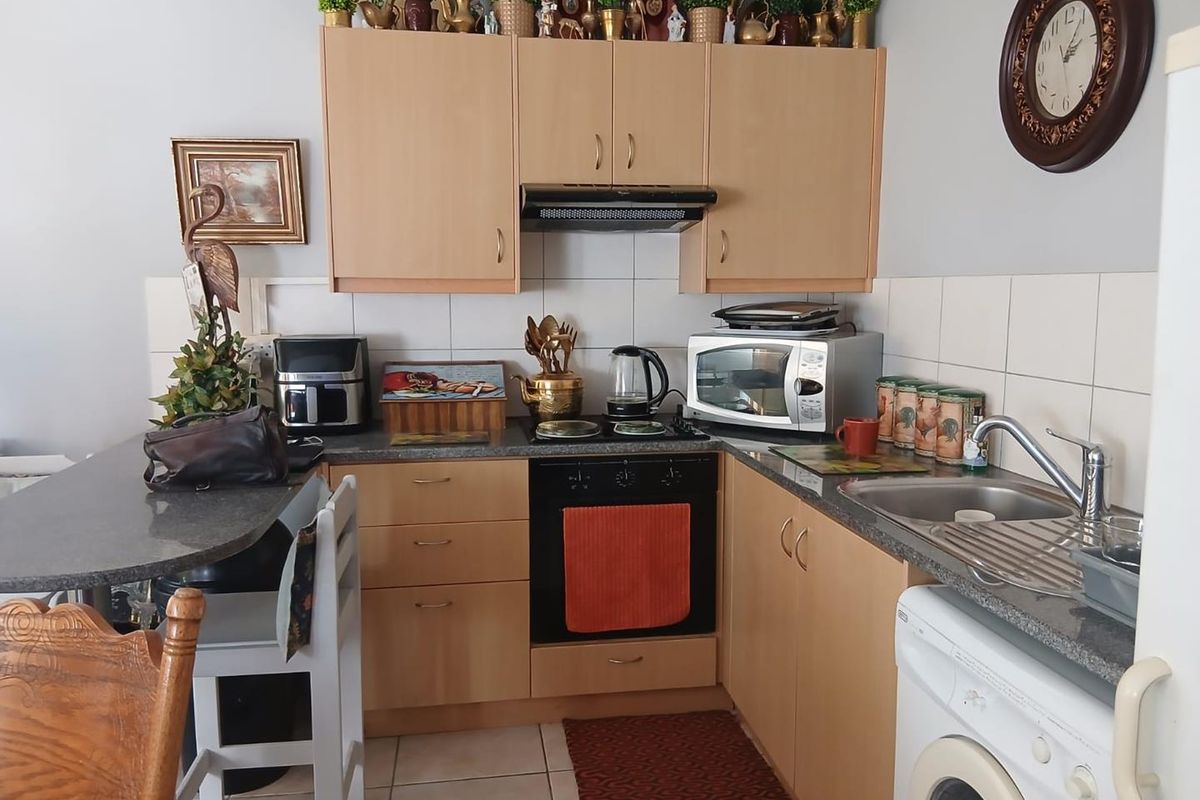 Compact kitchen featuring light wood cabinetry, laminate countertops, integrated oven, extractor fan, and a stainless steel sink with drainer.
