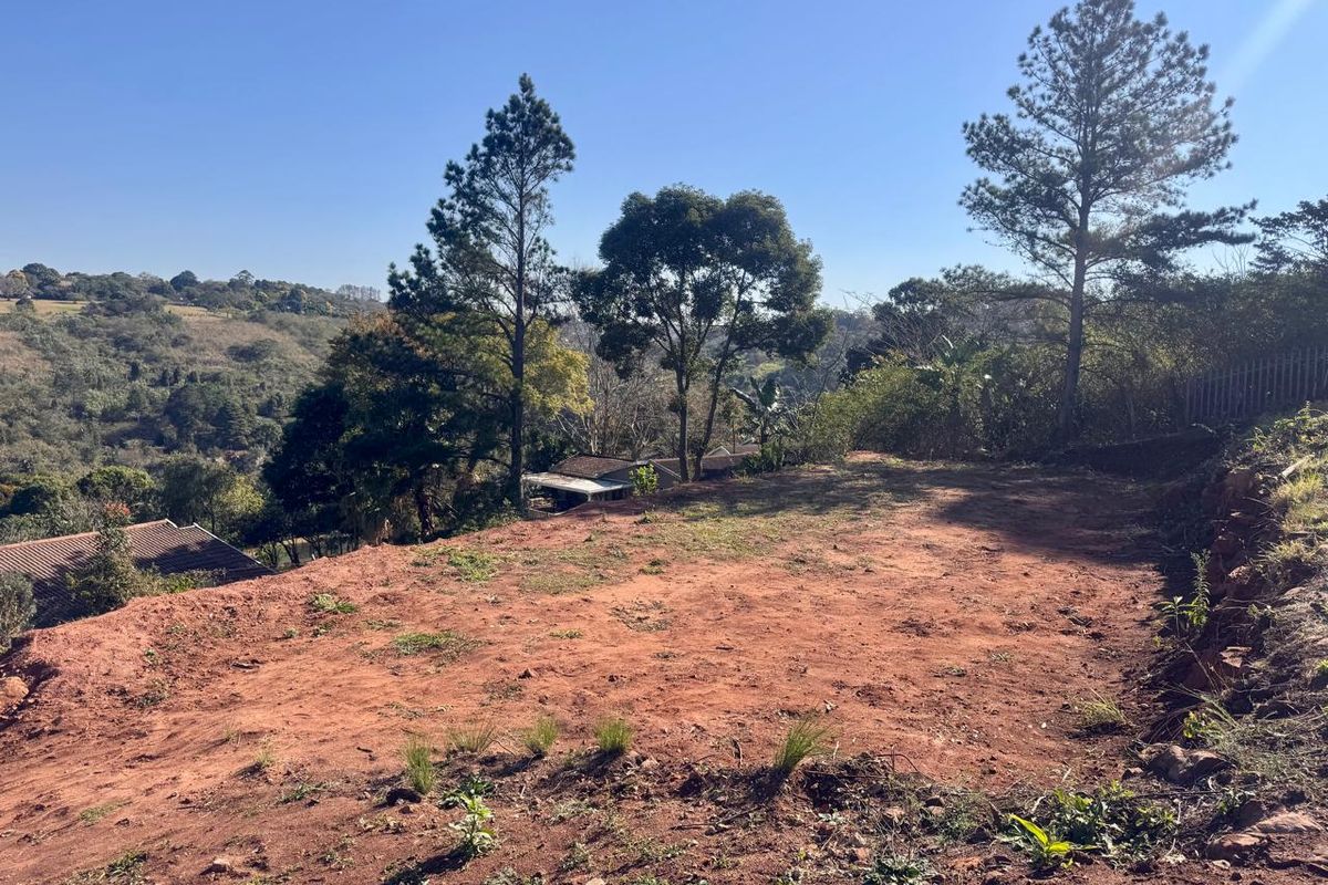 A view of a sloped, cleared residential plot featuring mature trees and surrounding landscape, ideal for future development.