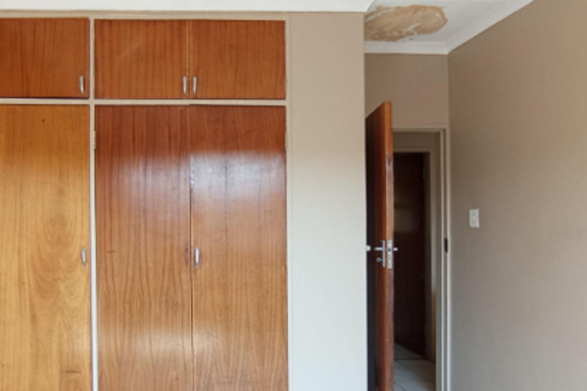 A bedroom featuring built-in wooden cupboards and a doorway leading to an adjacent space, showing signs of ceiling water damage.