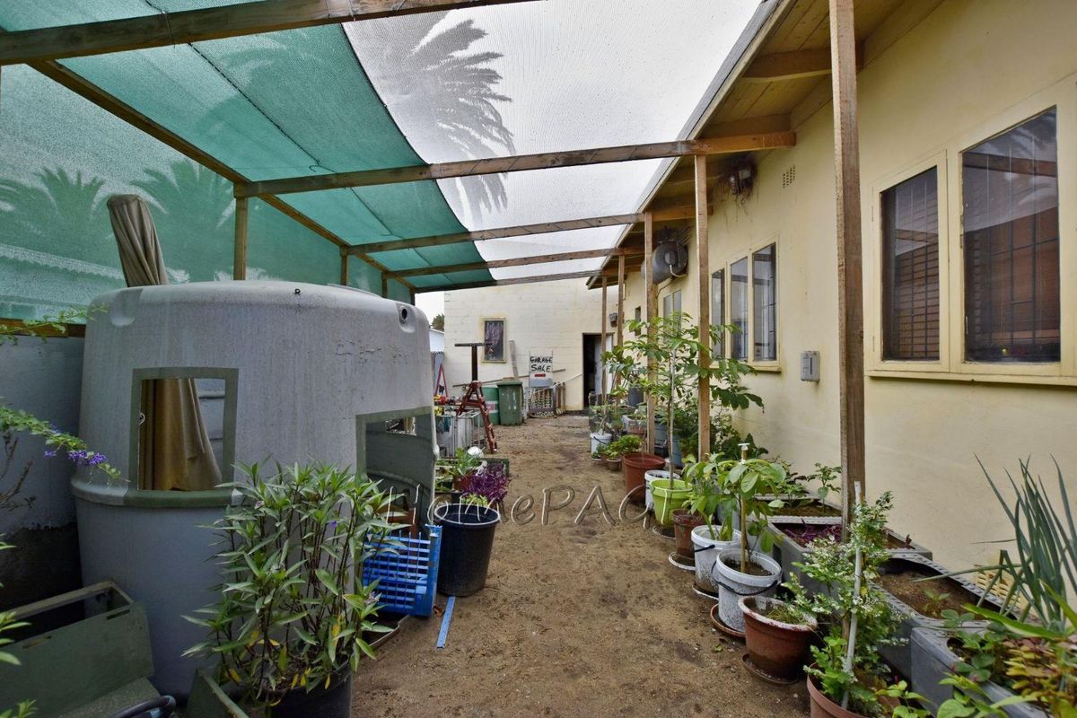 A side exterior area featuring a basic timber-framed shade cloth structure, providing covered outdoor space along the side of the house.