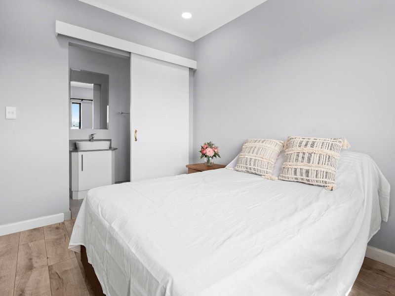 A well-maintained bedroom featuring laminate flooring, recessed lighting, and an adjoining en-suite bathroom with a modern vanity basin.