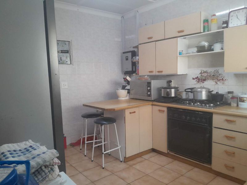 A functional kitchen featuring dated cabinetry, a built-in oven with gas hob, tiled splashbacks, and a small breakfast counter area.