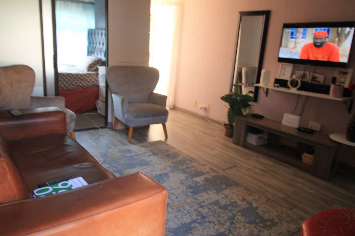 A living room area featuring laminate flooring and a view into an adjacent bedroom space.