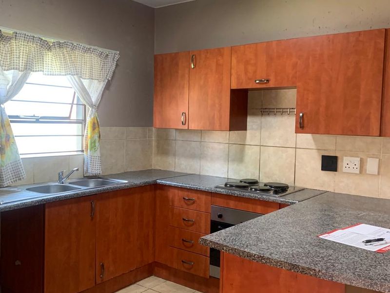 A functional kitchen featuring wood-look cabinetry, granite countertops, a built-in oven with hob, and tiled flooring, offering a practical layout for daily use.