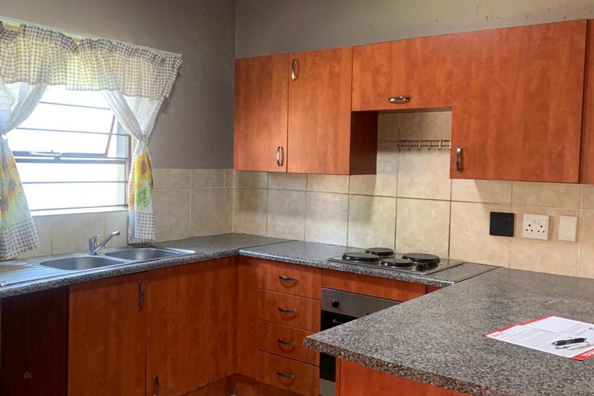 A functional kitchen featuring wood-look cabinetry, granite countertops, a built-in oven with hob, and tiled flooring, offering a practical layout for daily use.
